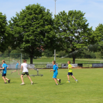 Leichtathleten laufen unter dem Rasensprenger und kühlen sich ab bei hochsommerlichen Temperaturen